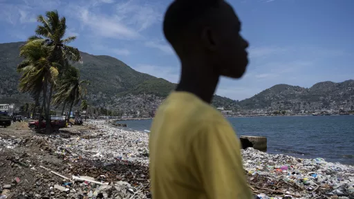 Silhouette of person in yellow shirt standing on beach looking toward bay