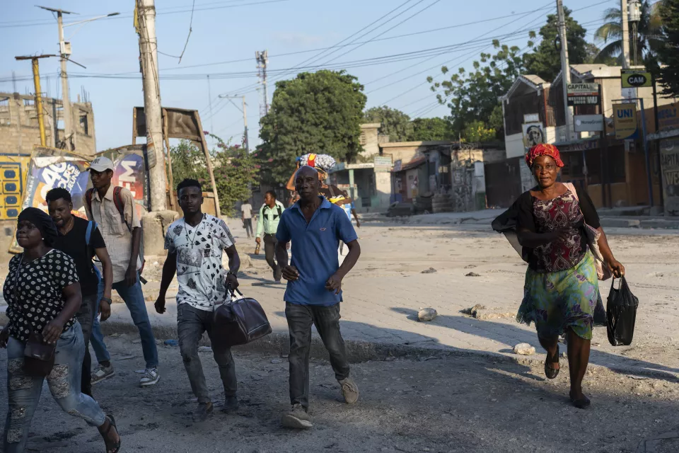 Group of people walking along urban street carrying bags and belongings