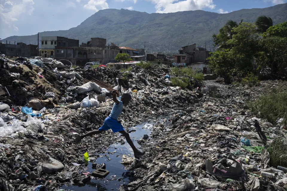 Child in blue shirt mid-leap over debris-filled waterway
