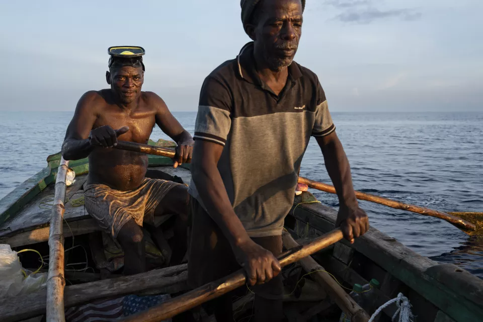 Two fishermen in wooden boat on calm ocean at dawn or dusk