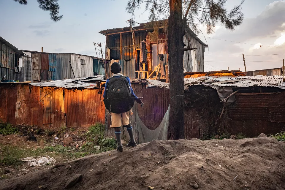 Young person with backpack viewed from behind standing on muddy ground