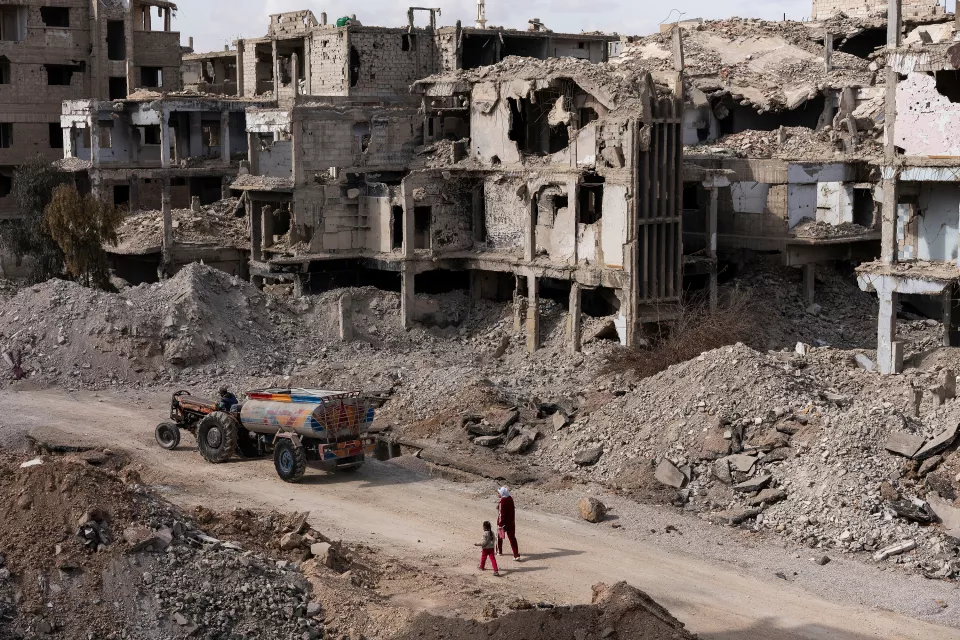 aerial view of a destroyed city street showing a woman and her child and a tractor 