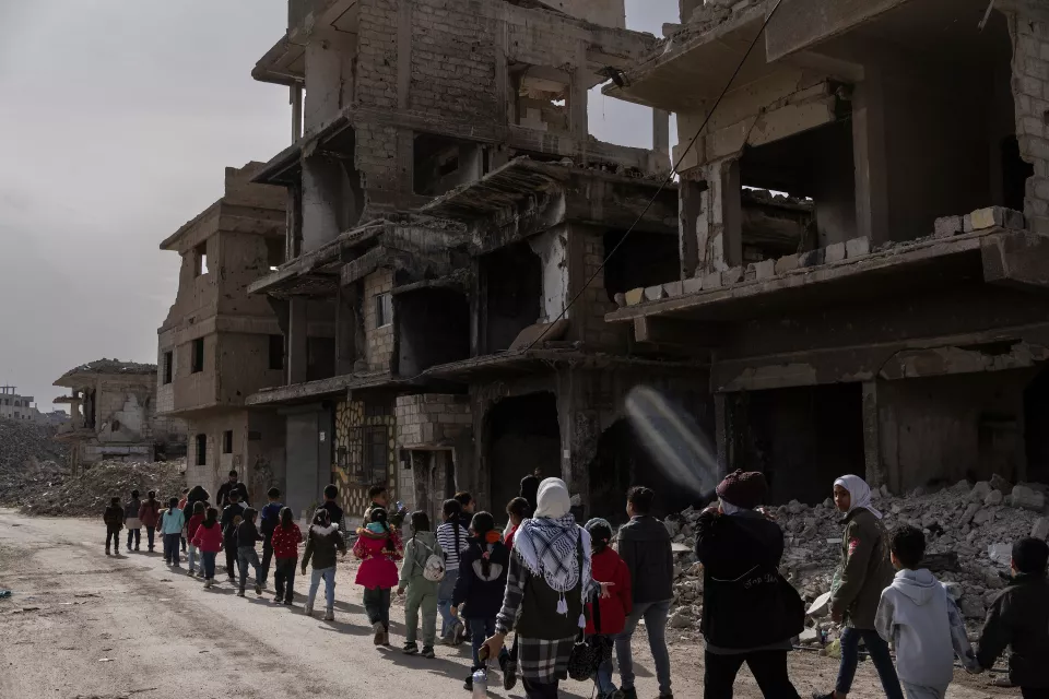 A line of children walk to school amid the ruins. 