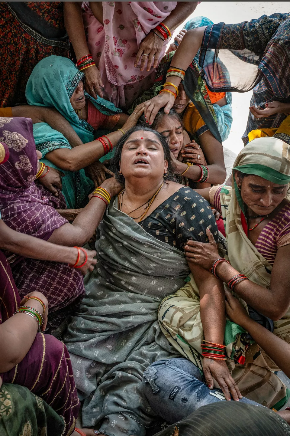 Close-up of a woman crying out in grief, surrounded by hands comforting her.
