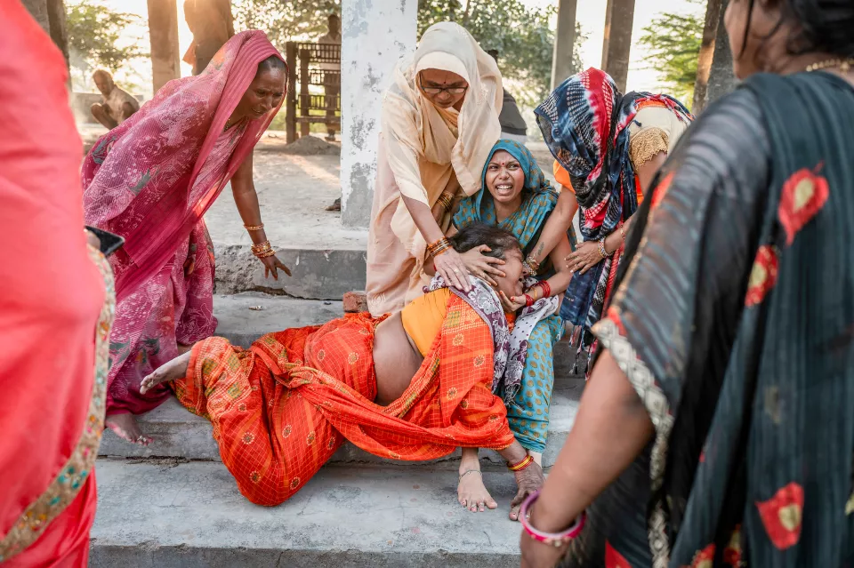 A grieving woman collapses on concrete steps while other women try to hold and support her.