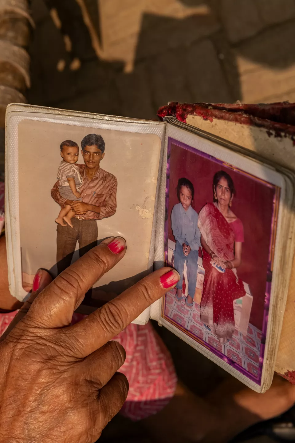 A hand points to old photographs in an album: a man holding a baby, and a girl sitting beside a woman.