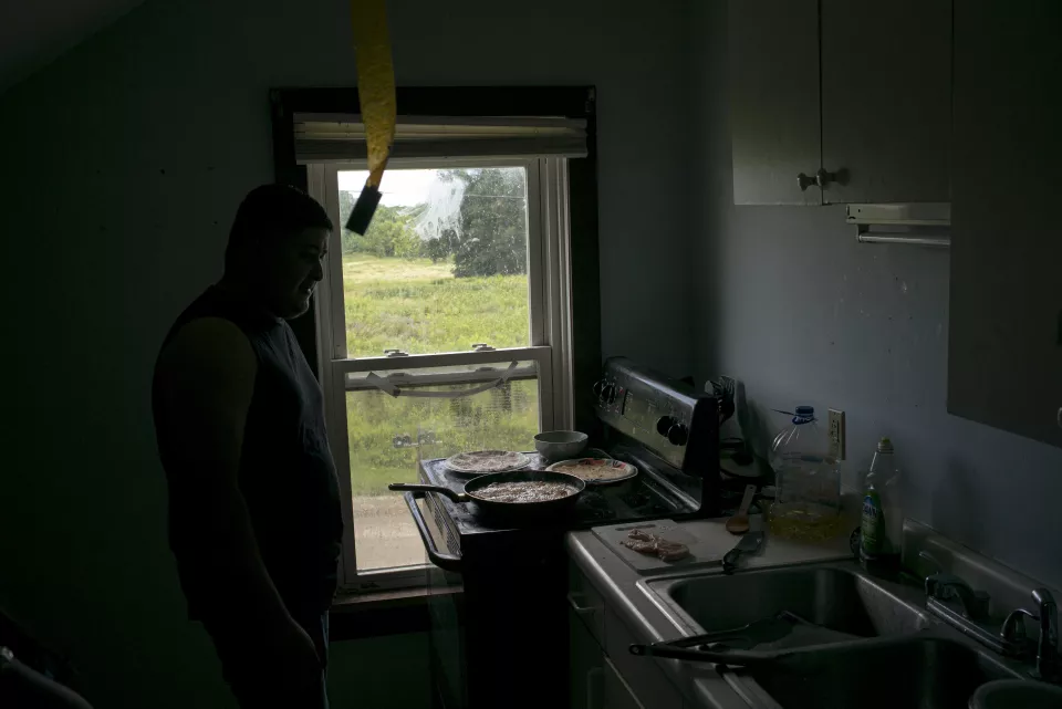 Silhouette of a man in a dim kitchen looking out the window, food cooking on the stove.