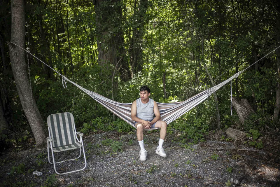 A young man sitting in a hammock in the woods.